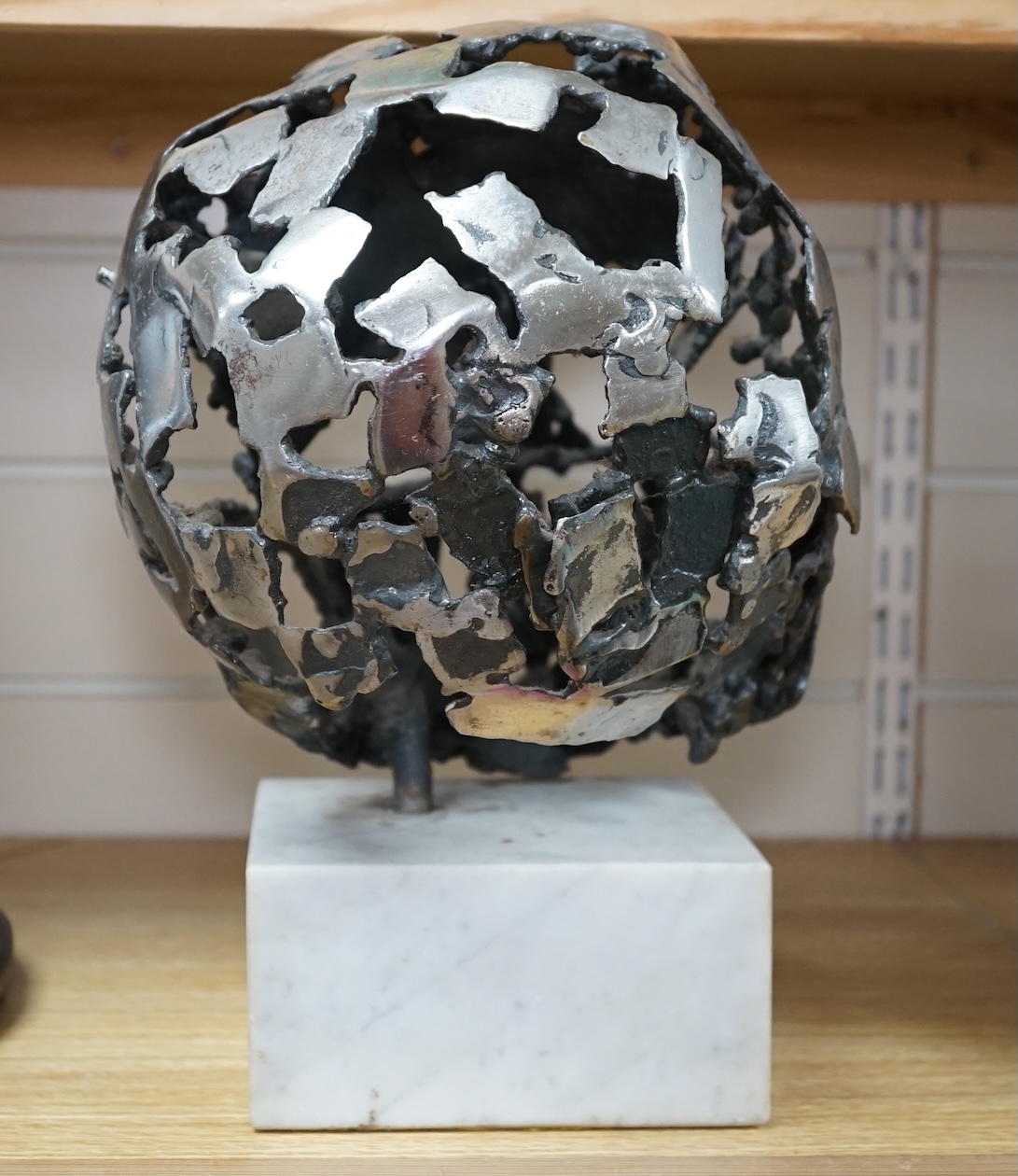 A modern polished steel skull, pierced and mounted on square white marble plinth, circa 1975, 31cm high. Condition - good, minor chipping